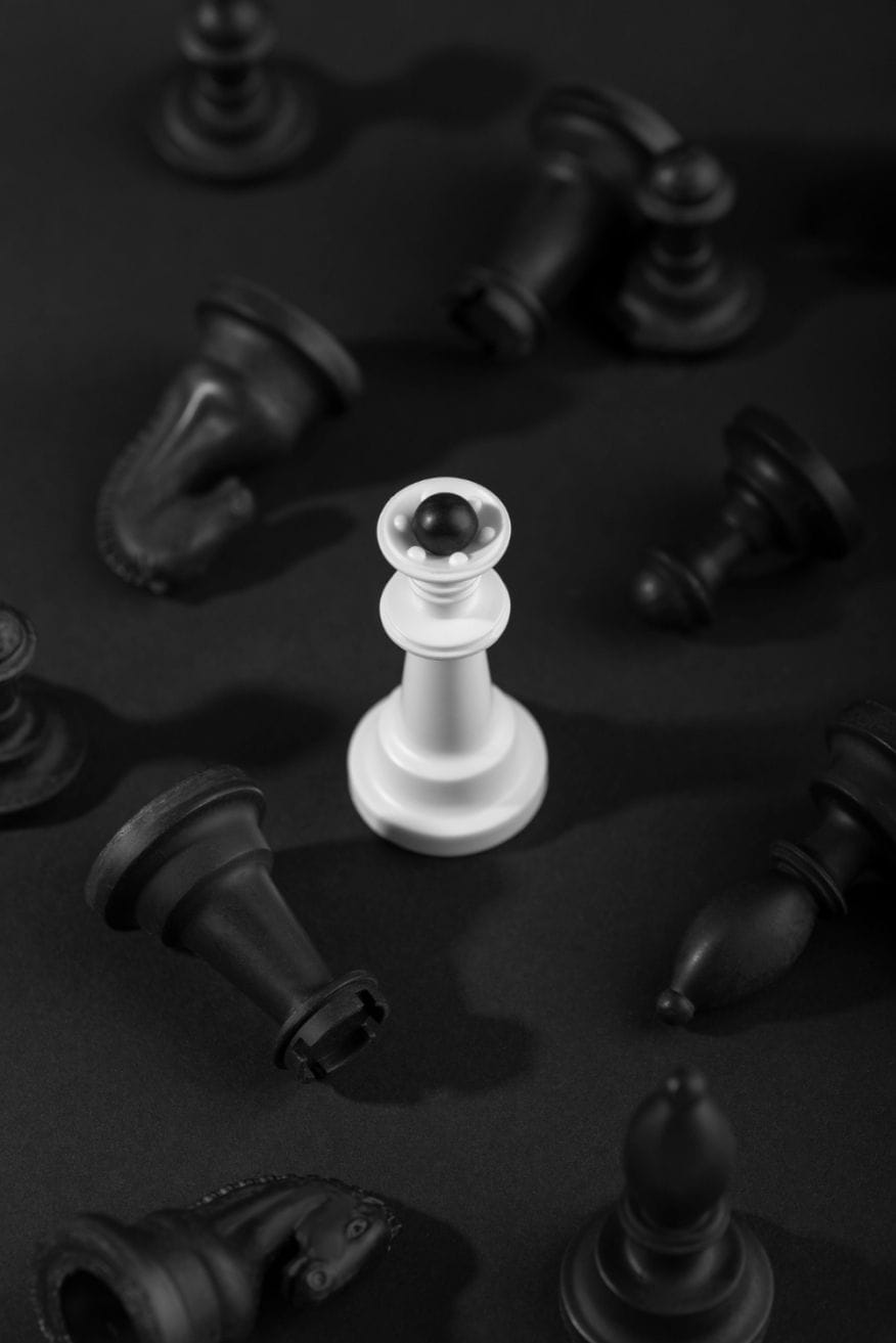 A single piece of white chess stands out from the other fallen black chess pieces