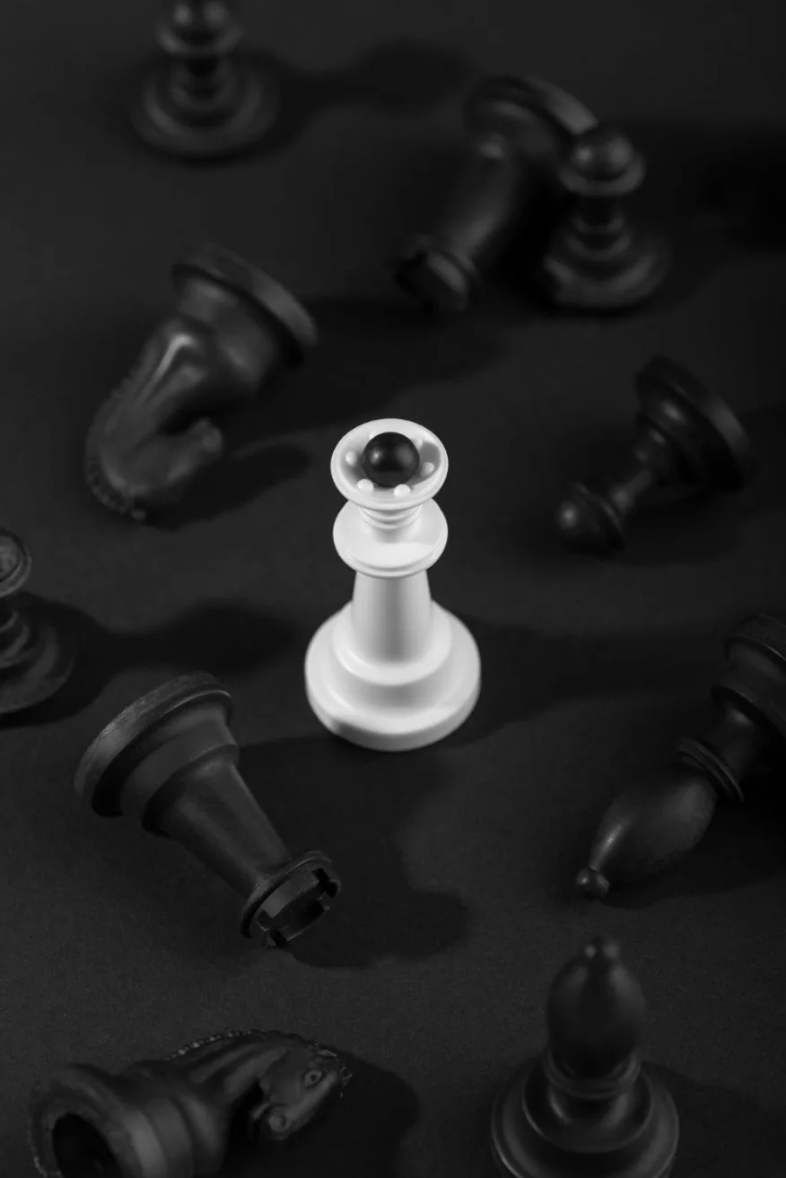 A single piece of white chess stands out from the other fallen black chess pieces